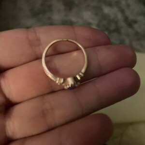 May include: A gold ring with a small purple gemstone in the center. The ring has a delicate design with small accents around the gemstone.