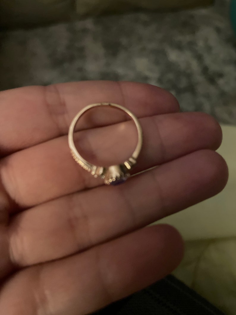 May include: A gold ring with a small purple gemstone in the center. The ring has a delicate design with small accents around the gemstone.