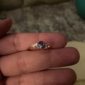 May include: A gold ring with a purple gemstone and small clear stones set in a floral design.