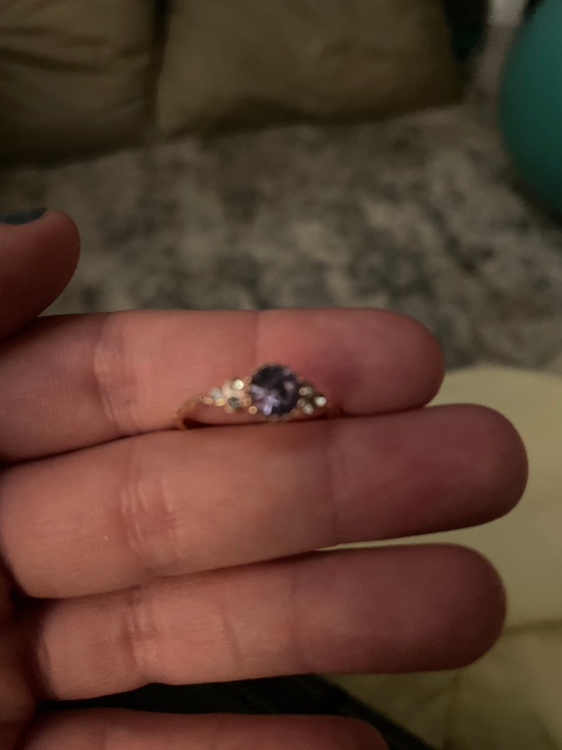 May include: A gold ring with a purple gemstone and small clear stones set in a floral design.