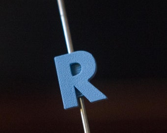 May include: A close-up of a bicycle wheel with a blue plastic letter 'R' attached to one of the spokes.
