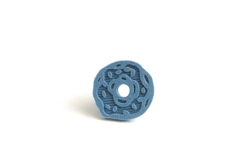 Peut inclure: Un charme bleu en forme de beignet avec un trou blanc au centre et un gla&ccedil;age blanc.