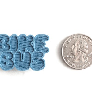 May include: A blue 3D printed pin with the words "Bike Bus" in a playful, rounded font.