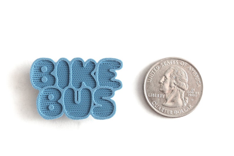 May include: A blue 3D printed pin with the words "Bike Bus" in a playful, rounded font.