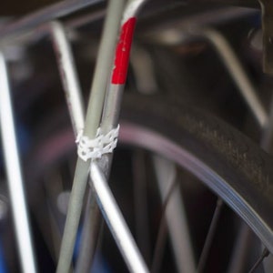 May include: Close-up of a silver bicycle frame with a red stripe and white tape. The bicycle has a black tyre with white lettering.