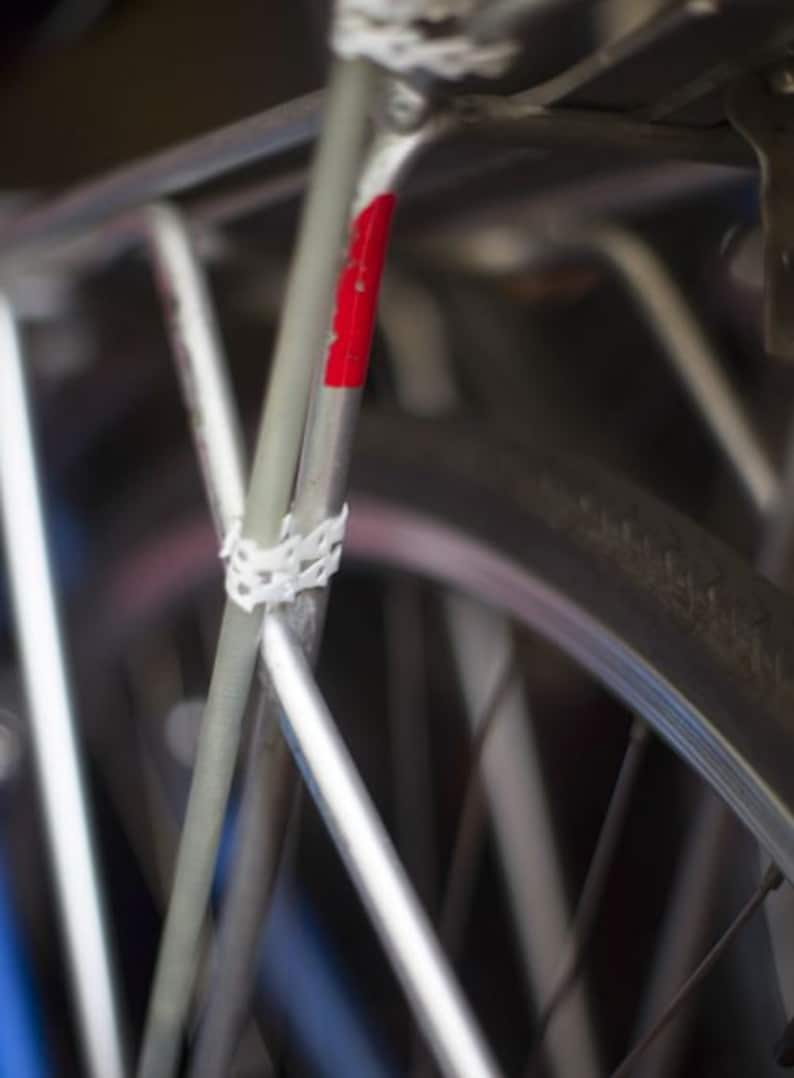 May include: Close-up of a silver bicycle frame with a red stripe and white tape. The bicycle has a black tyre with white lettering.