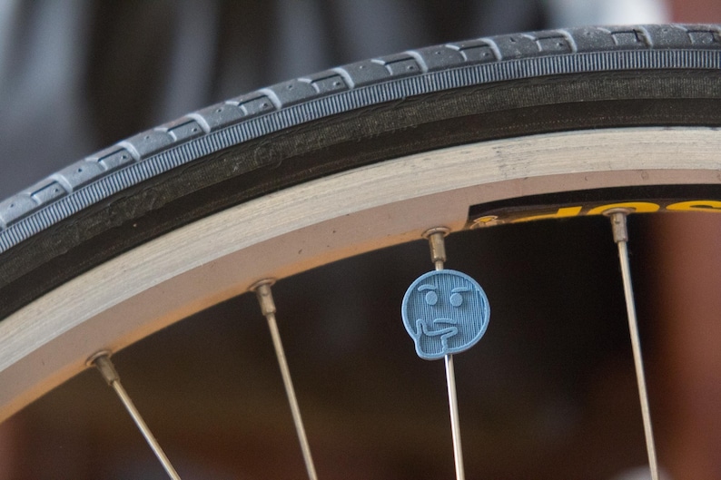Puede incluir: Primer plano de una rueda de bicicleta con una tapa de v&aacute;lvula de pl&aacute;stico azul en forma de emoji de cara pensante.