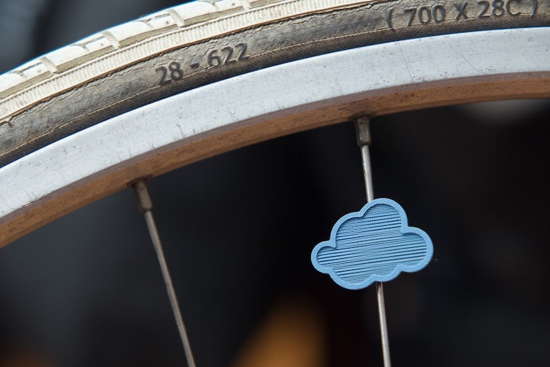 May include: Close-up of a bicycle wheel with a blue cloud-shaped valve stem cap. The tire is labeled "28 - 622 (700 x 28C)".