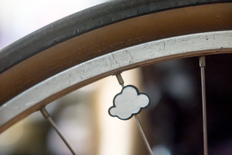 May include: Close-up of a bicycle wheel with a white cloud-shaped sticker on a spoke. The wheel is silver with a brown tire.