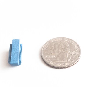 May include: A small blue book stack next to a US quarter dollar coin. The coin is silver in color and has the words "United States of America" and "Liberty" on it.