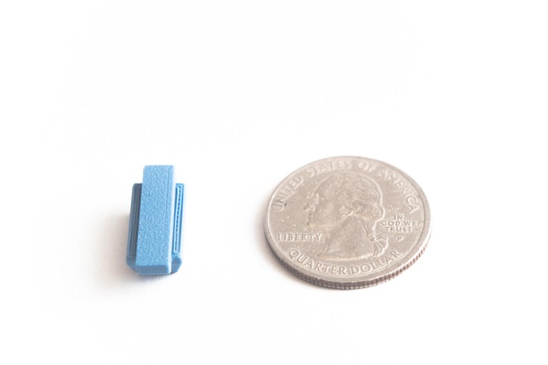 May include: A small blue book stack next to a US quarter dollar coin. The coin is silver in color and has the words "United States of America" and "Liberty" on it.