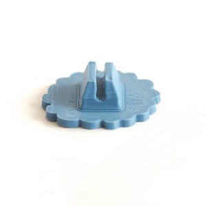 Puede incluir: Un soporte para tel&eacute;fono de color azul claro con un borde festoneado. El soporte tiene una base rectangular con una ranura central para sujetar un tel&eacute;fono en posici&oacute;n vertical. El soporte est&aacute; hecho de pl&aacute;stico y tiene un aspecto impreso en 3D.
