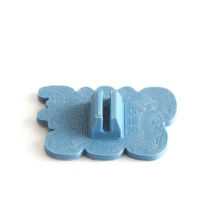 May include: A blue plastic 3D printed object with a wavy design and a slot in the center. The object is designed to hold a small item, such as a phone or a pen.