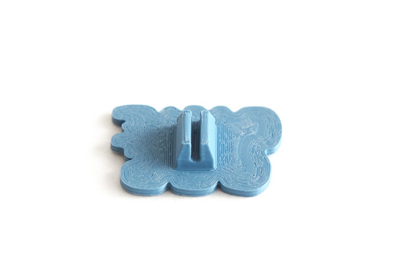 May include: A blue plastic 3D printed object with a wavy design and a slot in the center. The object is designed to hold a small item, such as a phone or a pen.