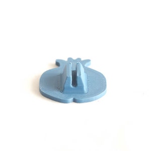 Pu&ograve; includere: Un supporto per telefono in plastica blu a forma di melograno. Il supporto ha una fessura sul retro per tenere un telefono.