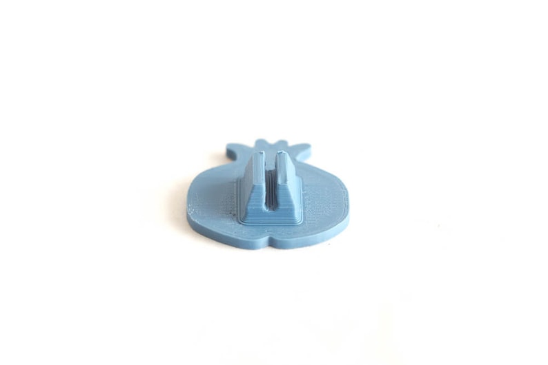 Pu&ograve; includere: Un supporto per telefono in plastica blu a forma di melograno. Il supporto ha una fessura sul retro per tenere un telefono.