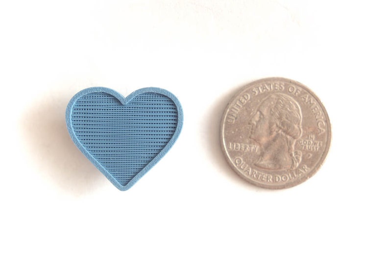 May include: A blue heart-shaped object with a textured surface, next to a US quarter.