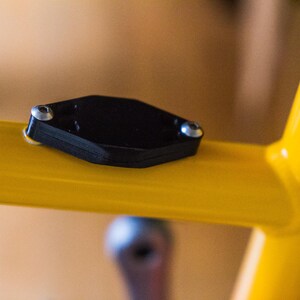 Bicycle AirTag Mount on the water bottle bosses of a yellow bike.