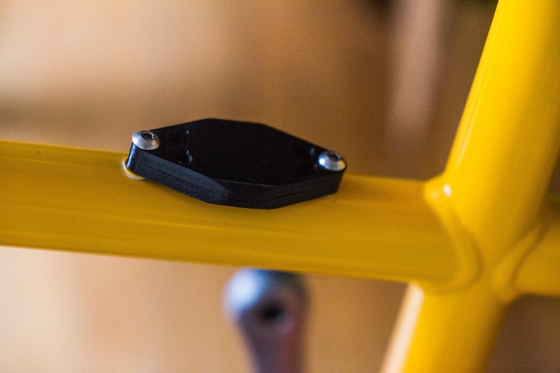 Bicycle AirTag Mount on the water bottle bosses of a yellow bike.