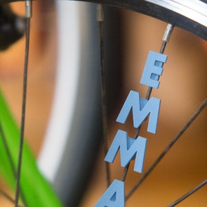 Op de afbeelding: Een fietswiel met de naam "EMMA" gespeld in blauwe letters op de spaken.