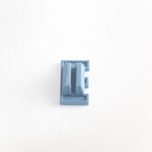 May include: A light blue plastic keycap with a double-height design. The keycap has a rectangular shape with a raised center section.