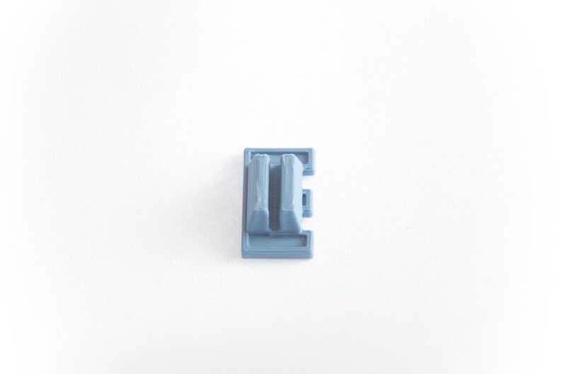 May include: A light blue plastic keycap with a double-height design. The keycap has a rectangular shape with a raised center section.