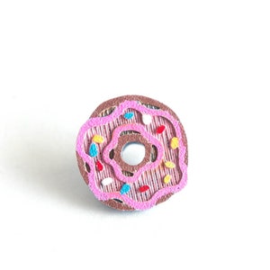Peut inclure: Un beignet glac&eacute; rose avec des p&eacute;pites color&eacute;es. Le beignet est en feutre et a un centre brun.