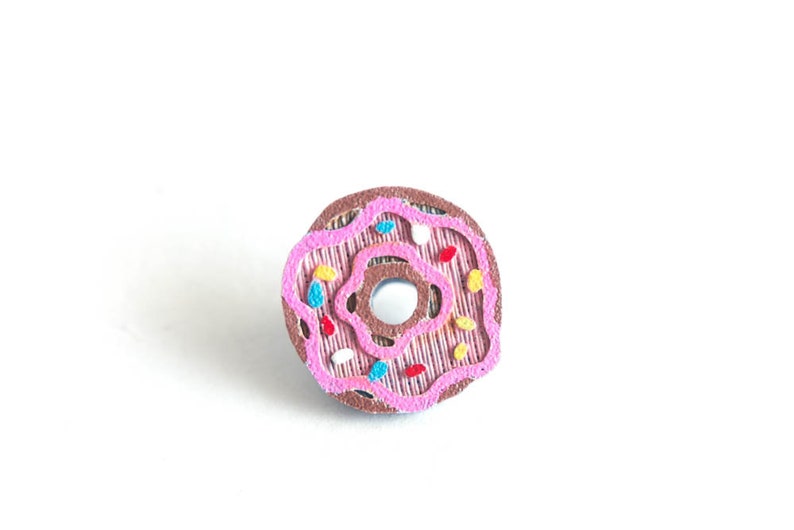 Peut inclure: Un beignet glac&eacute; rose avec des p&eacute;pites color&eacute;es. Le beignet est en feutre et a un centre brun.
