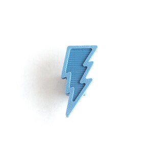 May include: A light blue lightning bolt shaped pin. The pin is made of a textured material.