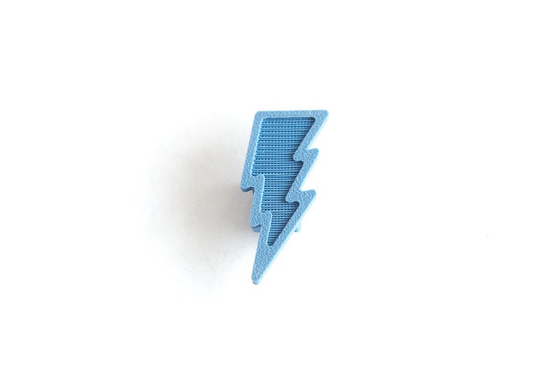 May include: A light blue lightning bolt shaped pin. The pin is made of a textured material.