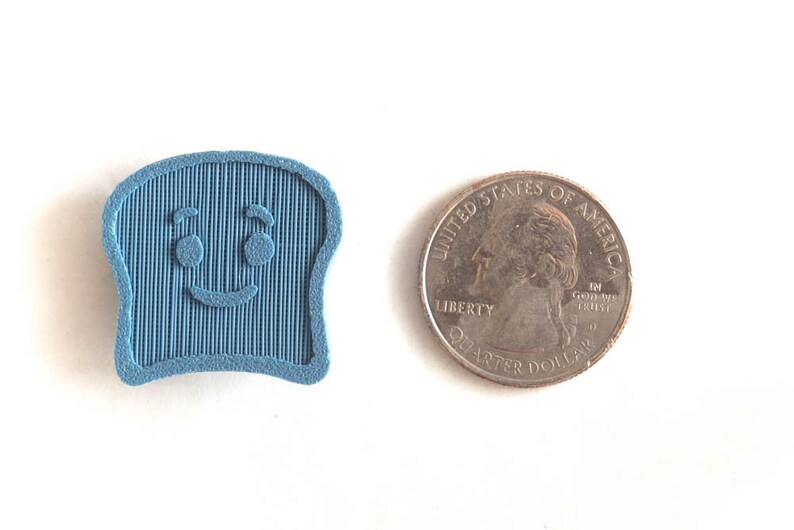 Puede incluir: Un objeto azul claro en forma de tostada sonriente con l&iacute;neas verticales, junto a una moneda de veinticinco centavos. El objeto tiene una cara de dibujos animados con dos ojos y una sonrisa curvada. La moneda es plateada.