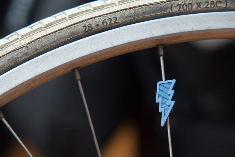 May include: A close-up of a bicycle wheel with a blue lightning bolt valve stem cap. The tire is labeled "28-622 (700 x 28C)".