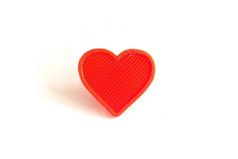 Pu&ograve; includere: Un oggetto a forma di cuore di colore rosso vivo in plastica. Il cuore ha una superficie testurizzata.
