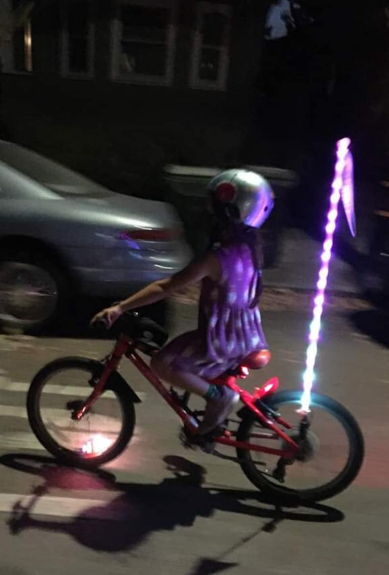 Child riding bicycle with LED glow staff and flag illuminating the rear.