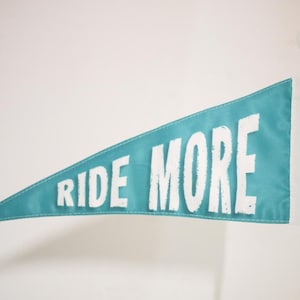 May include: A teal blue pennant flag with white text that reads "RIDE MORE".