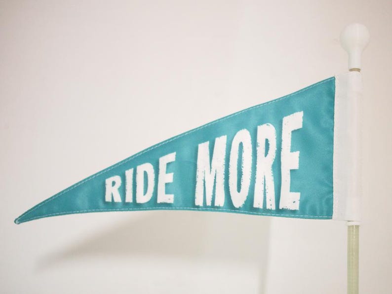 May include: A teal blue pennant flag with white text that reads "RIDE MORE".