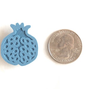 Pu&ograve; includere: Un ciondolo a forma di melograno stampato in 3D di colore azzurro chiaro, circa delle dimensioni di una moneta da 25 centesimi di dollaro americano.