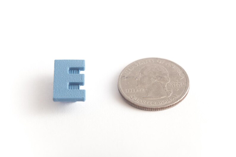 May include: A small, light blue plastic letter E, next to a US quarter for size comparison.