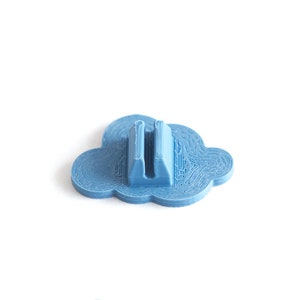 May include: A light blue plastic cloud-shaped object with a slot in the center. The object is designed to hold a small item, such as a pen or pencil.