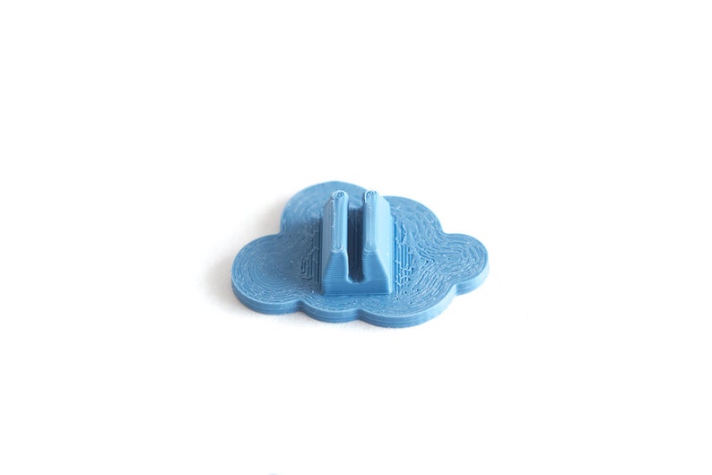 May include: A light blue plastic cloud-shaped object with a slot in the center. The object is designed to hold a small item, such as a pen or pencil.
