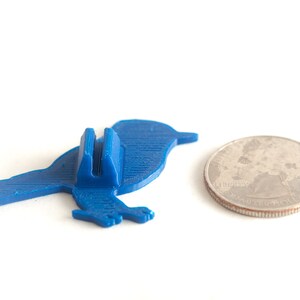 May include: A blue bird-shaped phone stand next to a quarter coin. The stand is made of plastic and has a slot to hold a phone. The quarter is silver and shows a profile of George Washington.