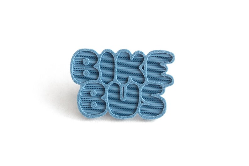 May include: A blue 3D printed pin with the text "Bike Bus" in a retro font.
