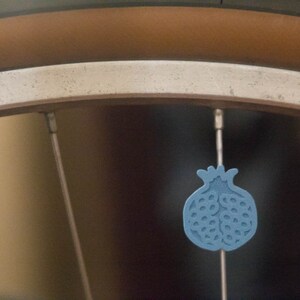 Pu&ograve; includere: Primo piano di una ruota di bicicletta con un ciondolo blu a forma di melograno appeso a un raggio.