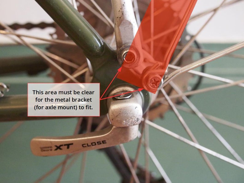 May include: Close-up of a bicycle rear derailleur with a silver lever labelled "XT CLOSE". The derailleur is attached to a green bicycle frame and a silver axle. The area around the axle must be clear for the metal bracket to fit.