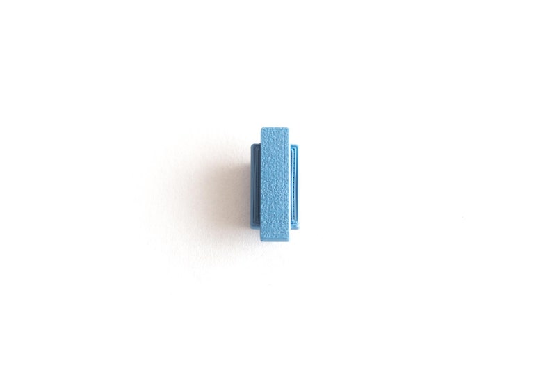 May include: A small, light blue plastic tile with a raised, textured surface.