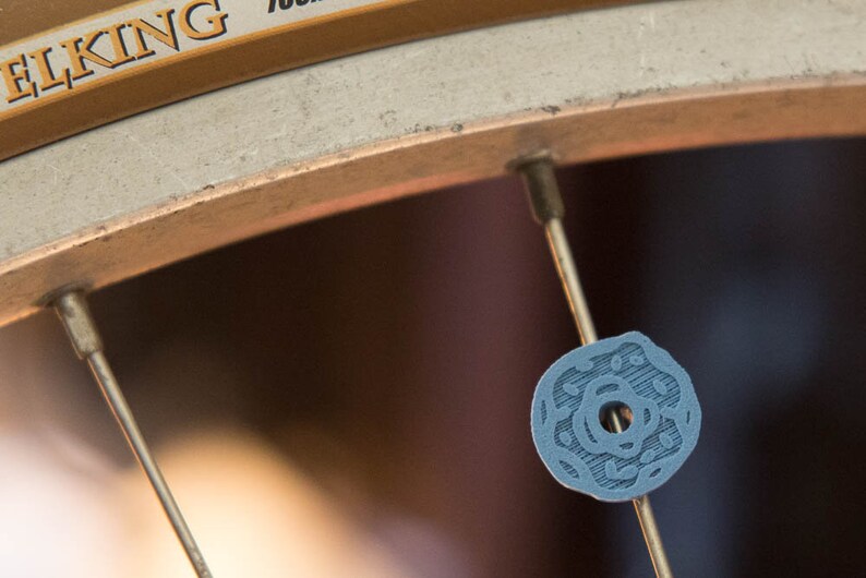 Peut inclure: Gros plan sur une roue de v&eacute;lo avec un capuchon de rayon bleu orn&eacute; d'un motif d&eacute;coratif. Le capuchon de rayon est fix&eacute; &agrave; un rayon argent&eacute;.