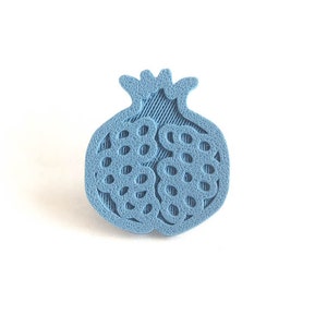 Pu&ograve; includere: Un design di melograno stampato in 3D di colore azzurro. Il melograno &egrave; dettagliato con una superficie testurizzata e un design ritagliato.