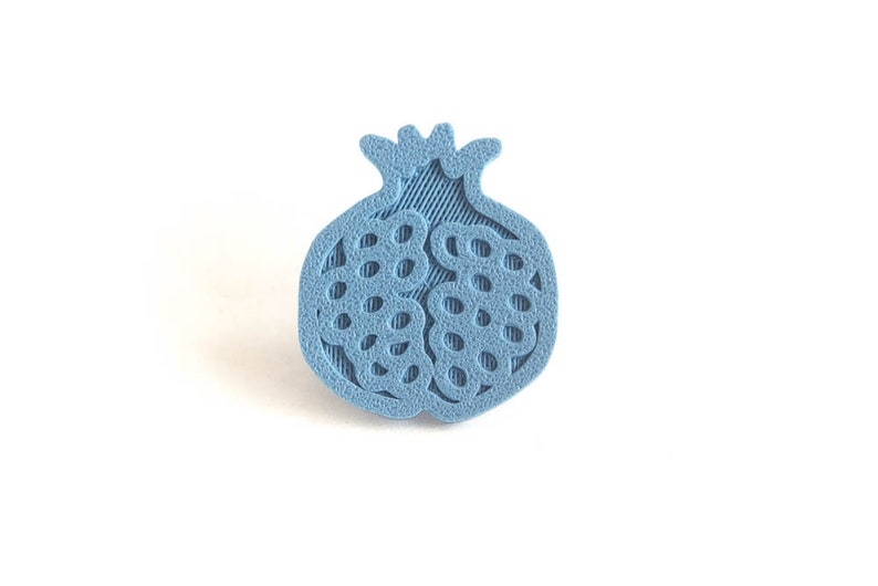 Pu&ograve; includere: Un design di melograno stampato in 3D di colore azzurro. Il melograno &egrave; dettagliato con una superficie testurizzata e un design ritagliato.