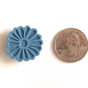Puede incluir: Un objeto azul claro en forma de flor con un dise&ntilde;o texturizado y detallado, junto a una moneda de veinticinco centavos estadounidense. El dise&ntilde;o del objeto presenta l&iacute;neas radiales y un c&iacute;rculo central.