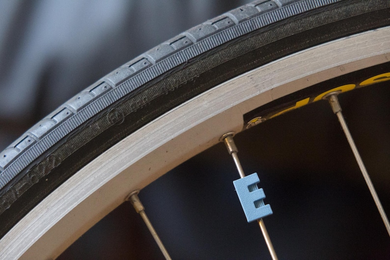 May include: Close-up of a bicycle wheel with a black tire and silver spokes. A blue spoke reflector is visible on one of the spokes.